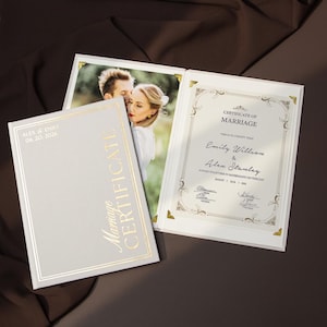 May include: A wedding certificate and a marriage certificate are displayed. The marriage certificate is white with gold accents and text. The wedding certificate is light gray with gold text and a photo of a couple. The date 06.20.2026 is visible.