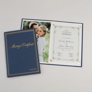 Peut inclure: Un dossier de certificat de mariage bleu marine avec le texte doré Marriage Certificate et 01 08 2026. Le dossier ouvert présente une photographie d'un couple et un certificat imprimé avec les noms Emily Willson et Alex Stanley.