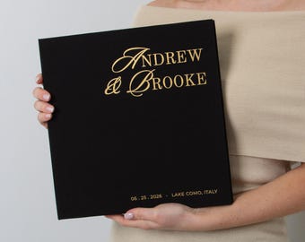 May include: A black photo album with gold lettering that reads "Andrew & Brooke" and the date "06.25.2026 Lake Como, Italy". The album is held by a person.