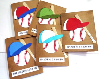 May include: Five handmade baseball-themed greeting cards with brown paper cardstock, white baseballs, and colorful baseball caps. The cards have the text "Hope your day is a home run" printed on them.