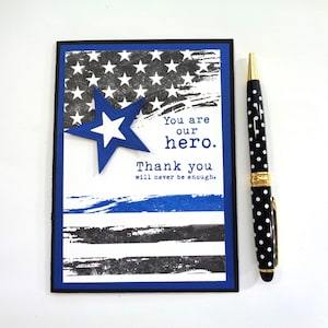 May include: A blue and white card with a distressed American flag design. The card has the text "You are our hero. Thank you will never be enough."