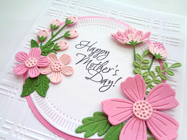 May include: A pink and green paper card with a circle of flowers and leaves around the text "Happy Mother's Day!"