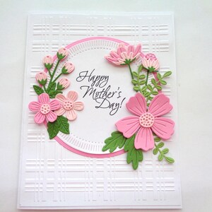 May include: A white card with a pink and green floral design. The card has a pink circle with the text "Happy Mother's Day!" in the center. The card has a white background with a subtle embossed pattern.