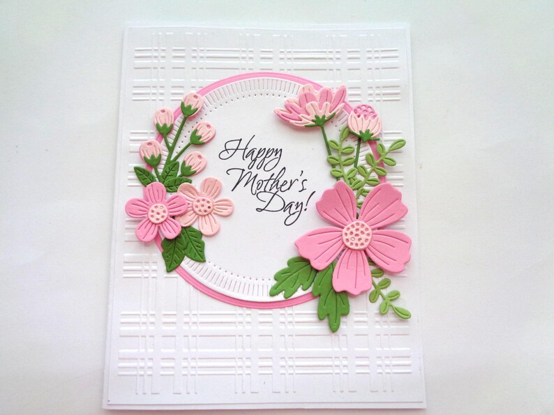 May include: A white card with a pink and green floral design. The card has a pink circle with the text "Happy Mother's Day!" in the center. The card has a white background with a subtle embossed pattern.