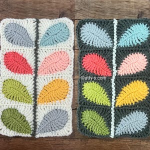 Puede incluir: Dos cuadrados de ganchillo con motivos de hojas. Uno es blanco con hojas grises, coral, rosas, amarillas, verdes y azules. El otro es gris oscuro con hojas azules, coral, rosas, amarillas, verdes y grises.