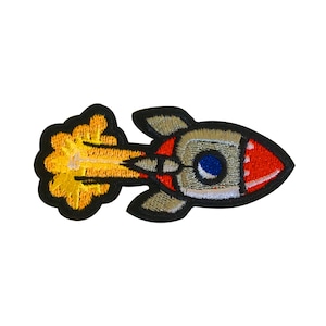 May include: A colorful embroidered patch of a cartoon rocket ship with a yellow flame shooting out the back. The rocket is gray, red, and blue.