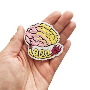 May include: An embroidered iron-on patch featuring a pink and yellow brain with a yellow electrical cord and a red plug.
