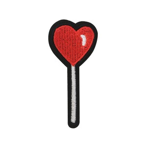 May include: Red heart-shaped lollipop on a stick with black and white stitching.