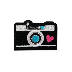 May include: Black and white embroidered camera patch with a blue lens and a pink heart.