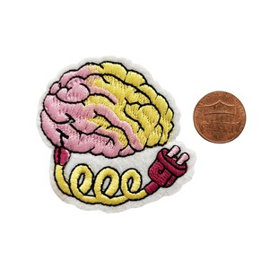 May include: An embroidered iron-on patch featuring a pink and yellow brain with a red and yellow electrical cord. The patch is about the size of a UK penny.