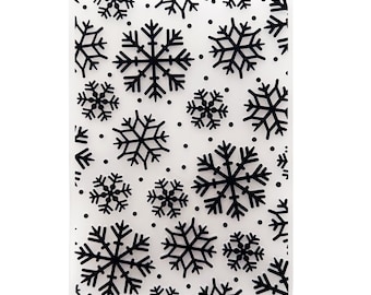 May include: A clear plastic sheet with a repeating pattern of black snowflakes and dots. This sheet is designed for crafting and can be used for scrapbooking, card making, and other projects.