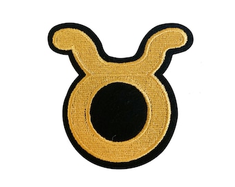 May include: Gold embroidered Taurus zodiac sign patch. The patch is outlined in black and has a black circle in the center.