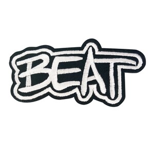 May include: Black and white embroidered patch with the word "BEAT" in a stylized font. The word is in white, outlined in black, and set against a black background.
