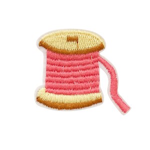 May include: A pink and yellow embroidered thread spool with a white background.
