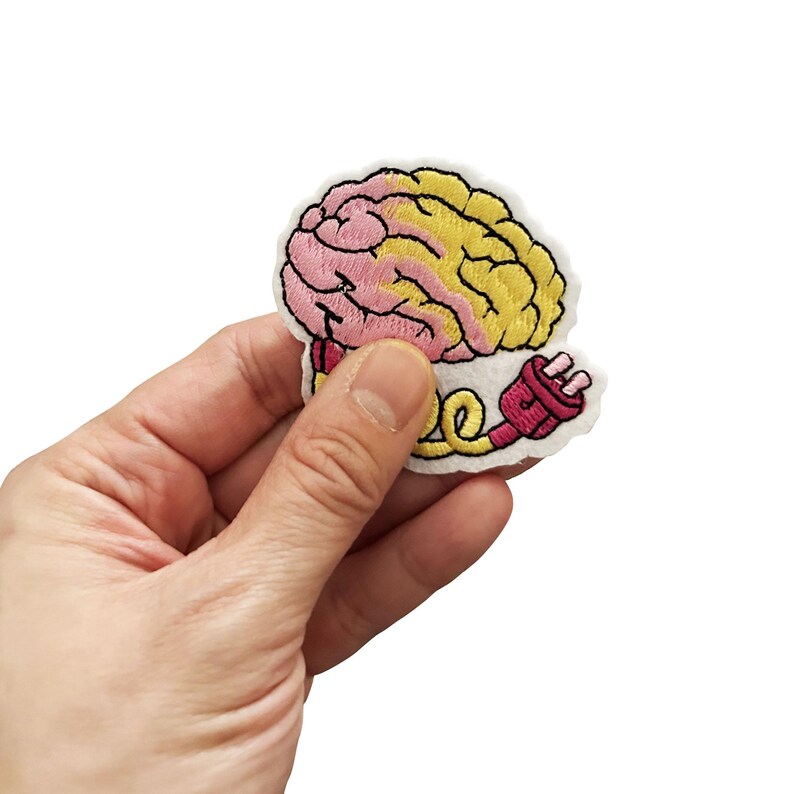 May include: An embroidered iron-on patch featuring a pink and yellow brain with a pink electrical cord and plug. The patch is on a white background.