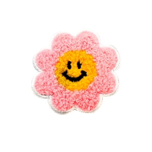 May include: A pink fuzzy flower with a yellow smiley face in the center. The flower has a white outline.