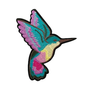 May include: Embroidered iron-on patch of a colorful hummingbird with pink, blue, and yellow accents. The hummingbird is facing right and has its wings spread out.