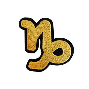 May include: Gold embroidered Capricorn zodiac sign patch with a black outline.