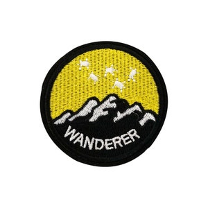 May include: A black and yellow embroidered patch with a mountain range and a constellation of stars. The text "WANDERER" is embroidered in white below the mountain range.