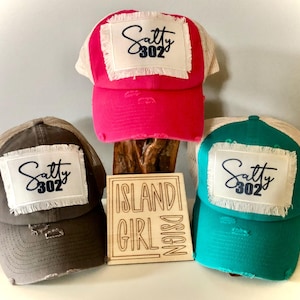 May include: Three trucker hats with a distressed look and a white patch with the text "Salty 302" in black. The hats are in pink, gray, and teal.