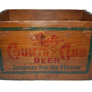 May include: Vintage wooden beer crate with the words "Goetz Country Club Beer" in red lettering. The crate has a green border and the phrase "...famous for its flavor". The crate is made of wood and has metal corner reinforcements.