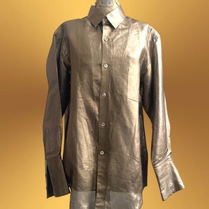 K&ouml;nnte beinhalten: Ein lang&auml;rmliges, metallisch goldenes Hemd mit Kn&ouml;pfen und einer einzigen Tasche auf der linken Brust.