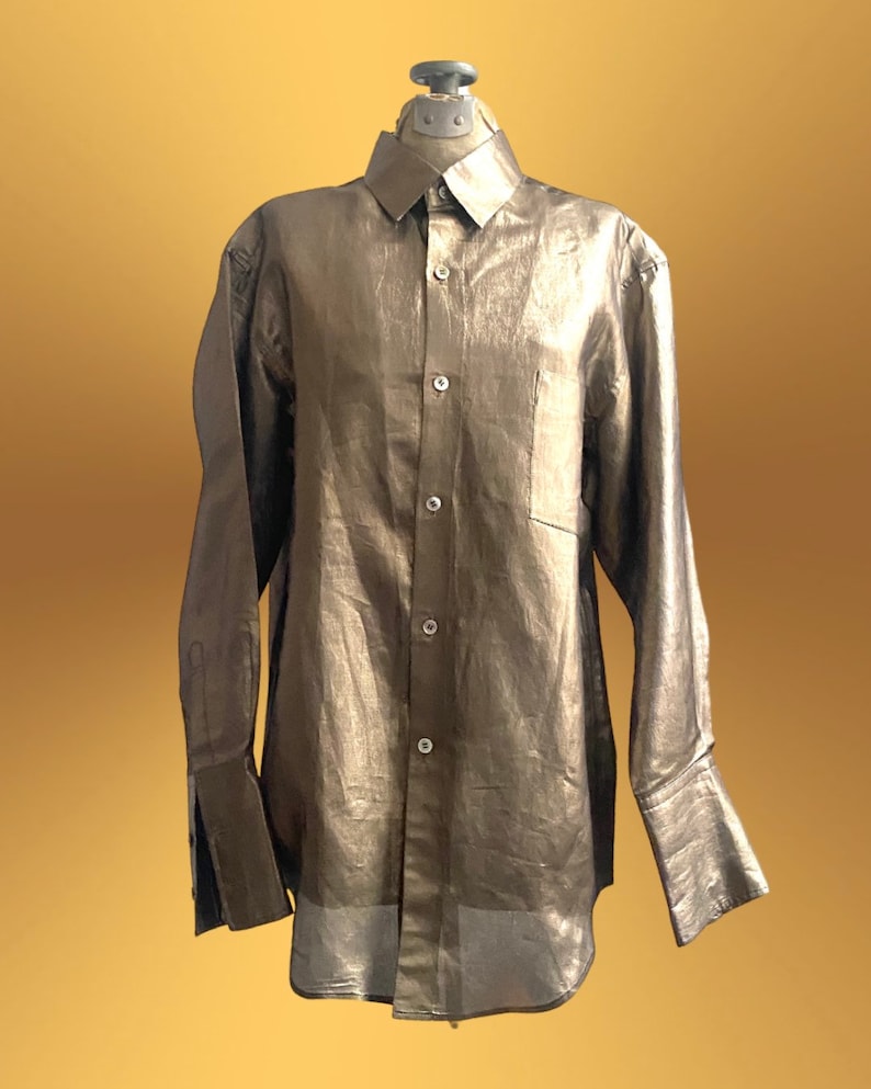 K&ouml;nnte beinhalten: Ein lang&auml;rmliges, metallisch goldenes Hemd mit Kn&ouml;pfen und einer einzigen Tasche auf der linken Brust.