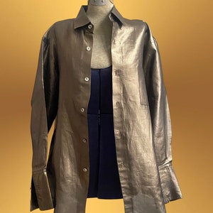 K&ouml;nnte beinhalten: Ein lang&auml;rmliges Hemd in Metallic-Gold mit Knopfleiste und einer einzigen Tasche auf der linken Seite. Das Hemd hat eine lockere Passform und ist aus einem leichten Stoff gefertigt.