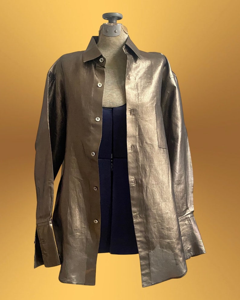 K&ouml;nnte beinhalten: Ein lang&auml;rmliges Hemd in Metallic-Gold mit Knopfleiste und einer einzigen Tasche auf der linken Seite. Das Hemd hat eine lockere Passform und ist aus einem leichten Stoff gefertigt.