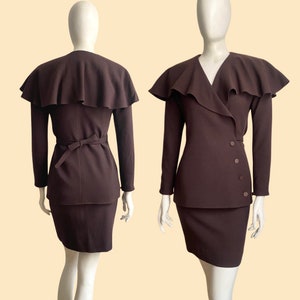 May include: A brown skirt suit with a ruffled collar and a wrap-style jacket. The jacket has a tie belt and buttons down the side.