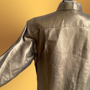 K&ouml;nnte beinhalten: Ein lang&auml;rmliges Hemd in metallischer Goldfarbe. Das Hemd hat einen Knopfkragenstil und eine glatte, gl&auml;nzende Oberfl&auml;che.