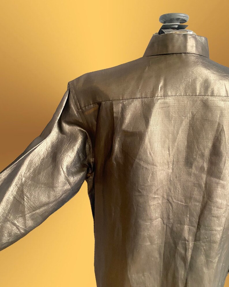 K&ouml;nnte beinhalten: Ein lang&auml;rmliges Hemd in metallischer Goldfarbe. Das Hemd hat einen Knopfkragenstil und eine glatte, gl&auml;nzende Oberfl&auml;che.