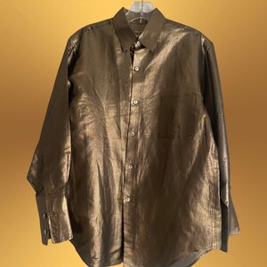 K&ouml;nnte beinhalten: Ein lang&auml;rmliges, goldfarbenes Hemd mit Kn&ouml;pfen und einer einzigen Tasche auf der linken Seite.