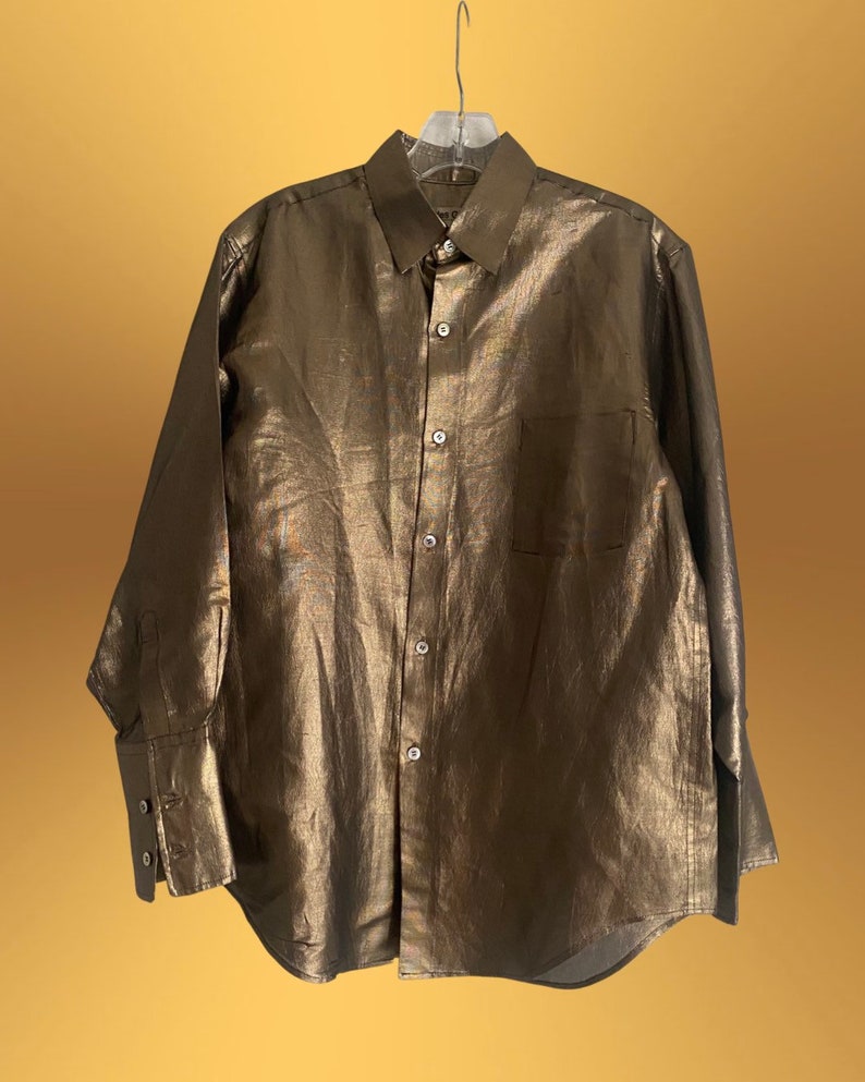 K&ouml;nnte beinhalten: Ein lang&auml;rmliges, goldfarbenes Hemd mit Kn&ouml;pfen und einer einzigen Tasche auf der linken Seite.