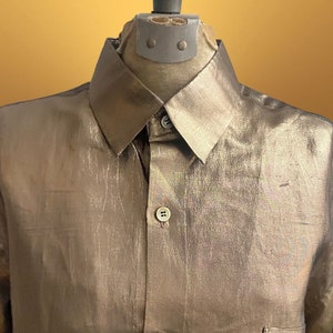 K&ouml;nnte beinhalten: Ein lang&auml;rmliges Hemd in Metallic-Gold mit Knopfleiste und einer einzigen Tasche auf der linken Seite.