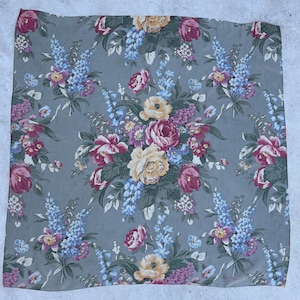 May include: A square, floral-patterned fabric in shades of gray, pink, yellow, and blue. The design features bouquets of roses, other flowers, and foliage. The fabric has a vintage aesthetic.