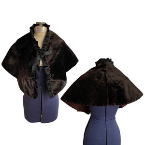 May include: A brown velvet cape with a ruffled collar and a black ribbon tie. The cape is shown on a dress form.