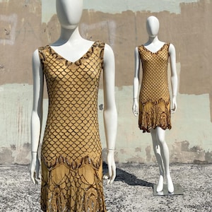 May include: A sleeveless gold dress featuring a V-neckline and a repeating scalloped pattern created with dark brown and metallic sequins. The garment has a drop-waist silhouette with intricate beaded detailing along the hemline and bodice.
