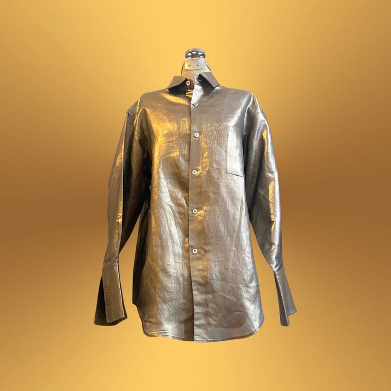 K&ouml;nnte beinhalten: Ein goldfarbenes, metallisches Hemd mit Kn&ouml;pfen, langen &Auml;rmeln und einer Tasche auf der linken Seite.
