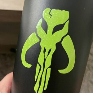 May include: A black water bottle with a green glitter Mandalorian symbol.