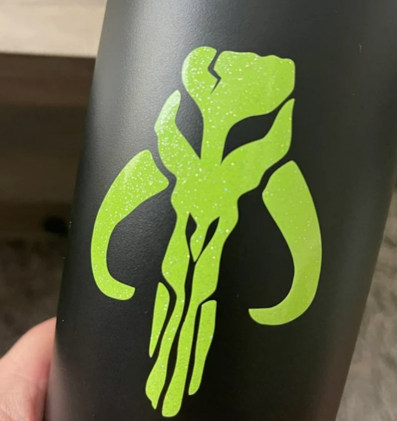 May include: A black water bottle with a green glitter Mandalorian symbol.
