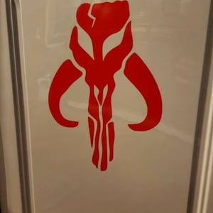 May include: A red Mandalorian symbol, also known as the "Death Watch" symbol, is displayed on a white surface.