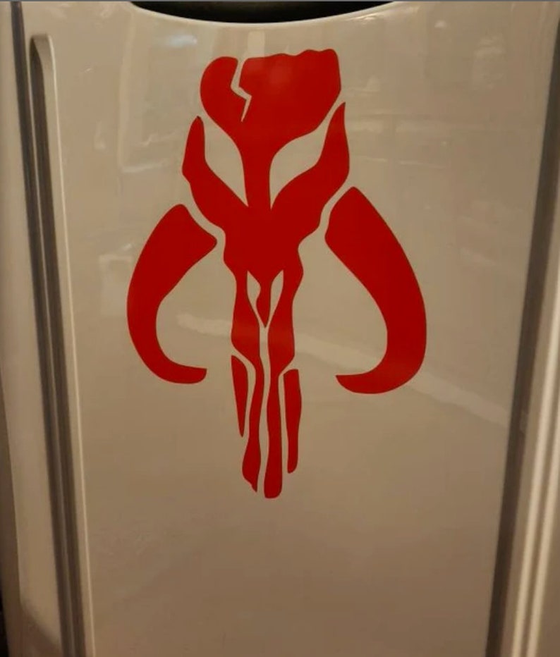 May include: A red Mandalorian symbol, also known as the "Death Watch" symbol, is displayed on a white surface.