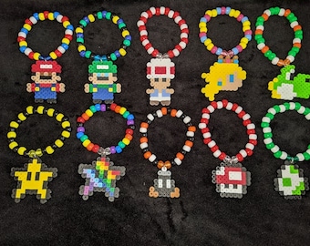 May include: Twelve colorful beaded bracelets with pixelated Super Mario Bros. character charms. The charms include Mario, Luigi, Toad, Princess Peach, Yoshi, a star, a rainbow, a mushroom, a Goomba, and a question block.