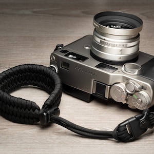 Può includere: Una macchina fotografica argentata con un cinturino in pelle nera e un obiettivo argentato con la scritta "Zeiss" su di esso.