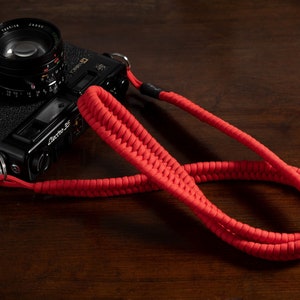May include: A black camera with a red camera strap. The camera has a lens with a black cap and the text "Electra 35" on the side.