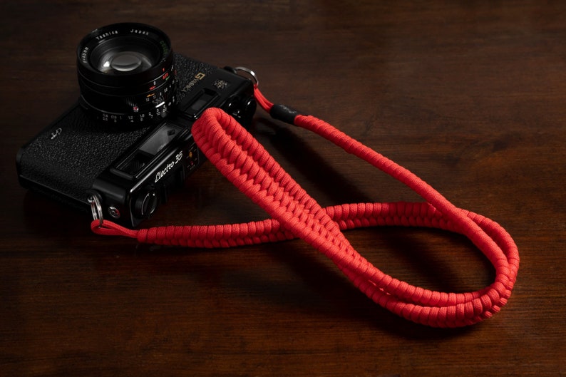 May include: A black camera with a red camera strap. The camera has a lens with a black cap and the text "Electra 35" on the side.
