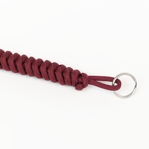 May include: A maroon paracord keychain with a silver metal ring.