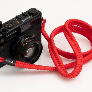 May include: A black 35mm film camera with a red braided camera strap. The camera has a lens with a silver ring and the text "Electra 35" on the top.