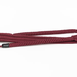 May include: A maroon braided camera strap with metal rings at each end.